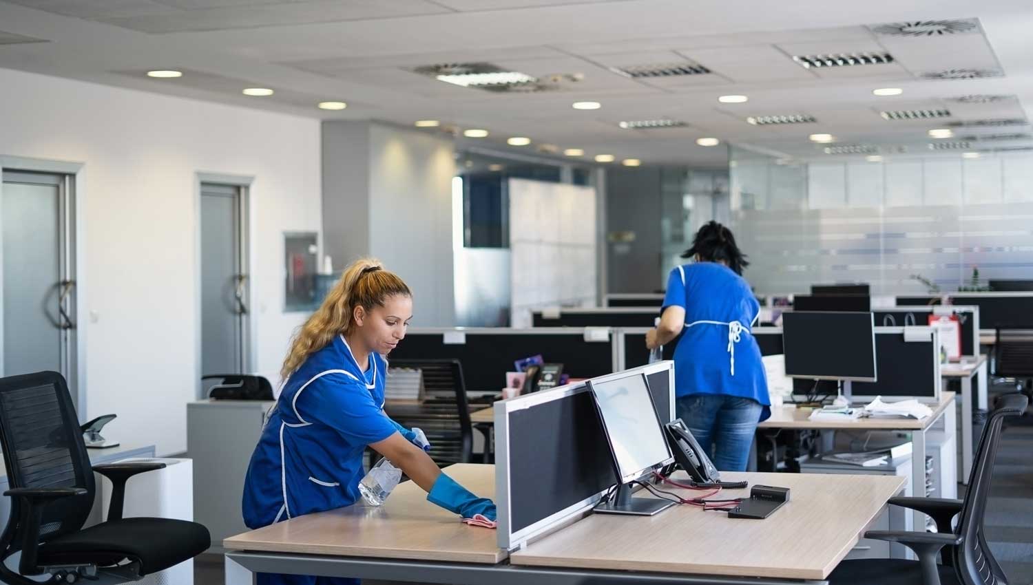 Uniformed cleaning crew sanitizing desks in an open-plan office