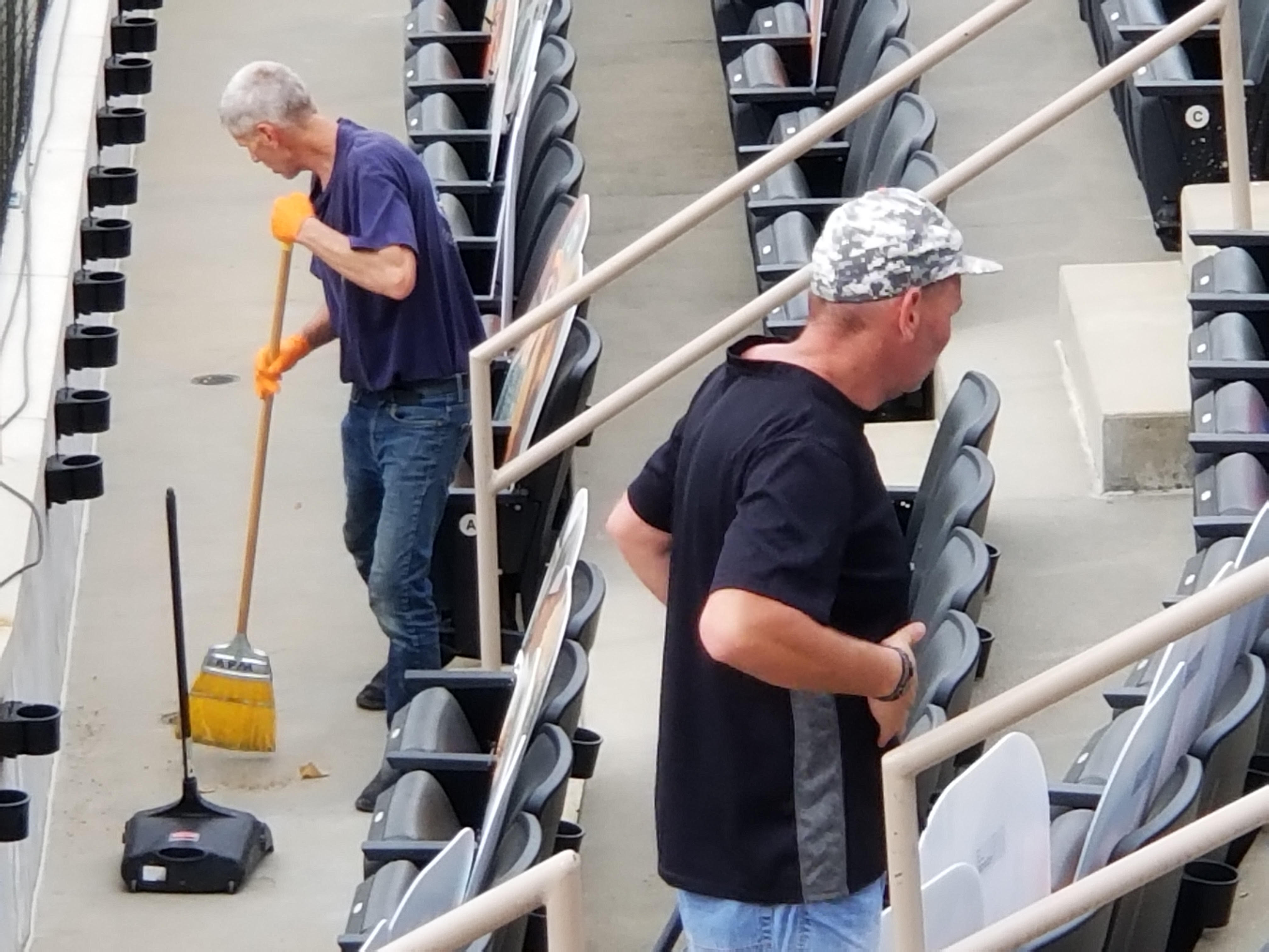Two crew members clearing debris from arena seating aisles